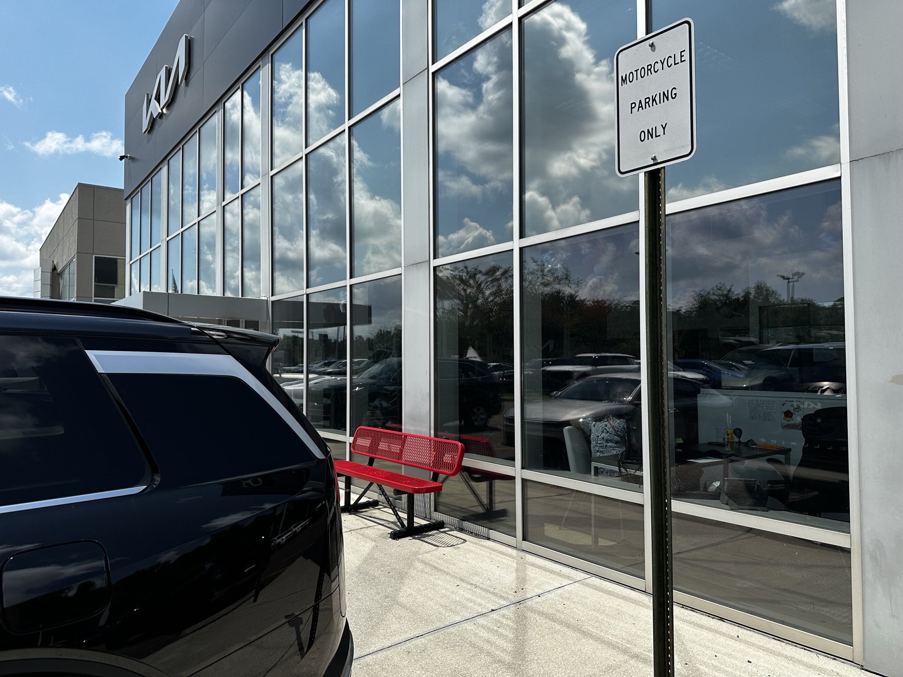 Dealership showroom exterior with tinted curtain-wall glass reflecting the sky and parked cars